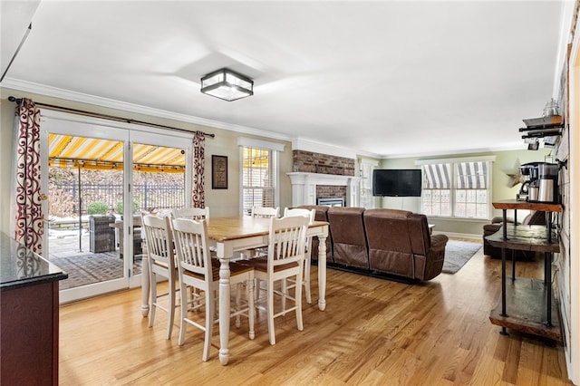 dining room with ornamental molding, a fireplace, light hardwood / wood-style flooring, and a wealth of natural light