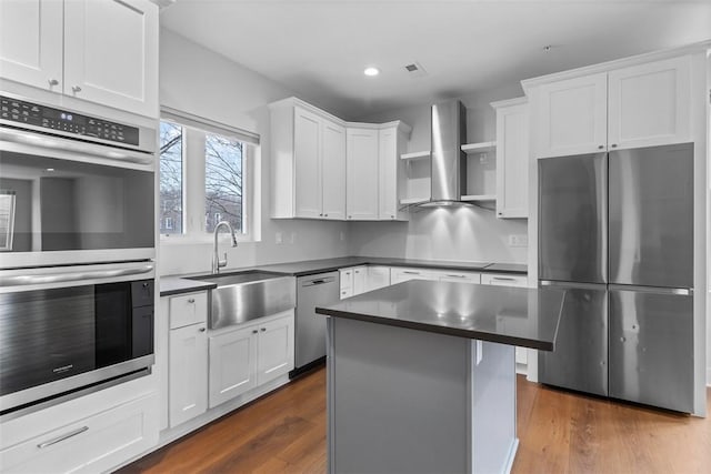 kitchen with sink, white cabinetry, stainless steel appliances, a center island, and wall chimney exhaust hood