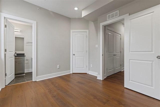 unfurnished bedroom with ensuite bath and dark wood-type flooring