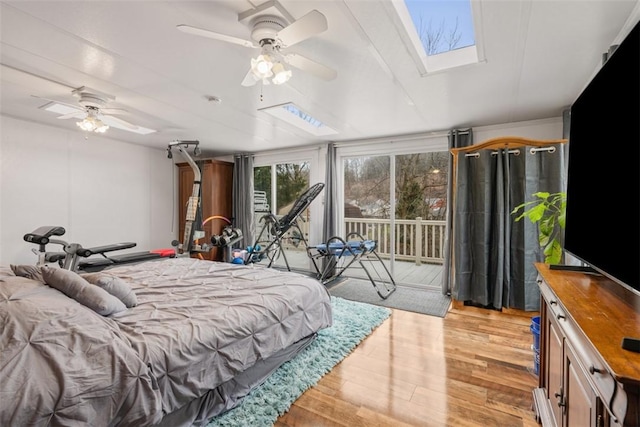 bedroom featuring ceiling fan, a skylight, light hardwood / wood-style flooring, and access to outside