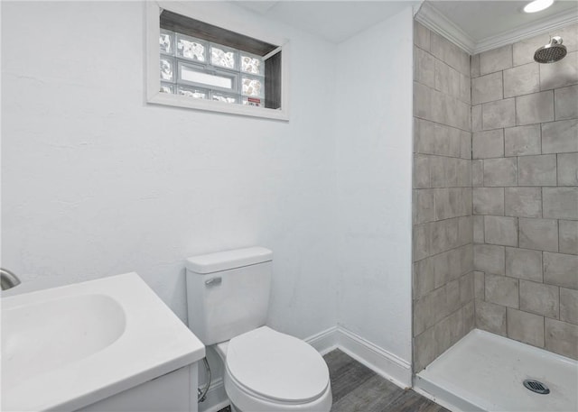 bathroom featuring crown molding, hardwood / wood-style floors, tiled shower, vanity, and toilet