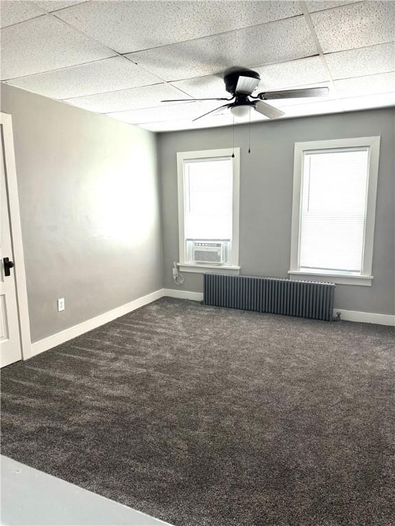 carpeted spare room with a drop ceiling, radiator heating unit, and ceiling fan