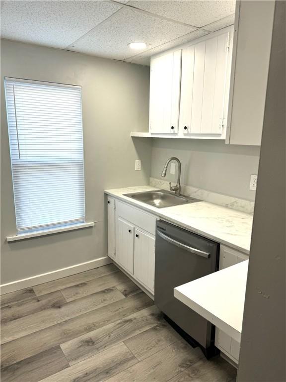 kitchen featuring sink, light hardwood / wood-style flooring, stainless steel dishwasher, white cabinets, and a drop ceiling