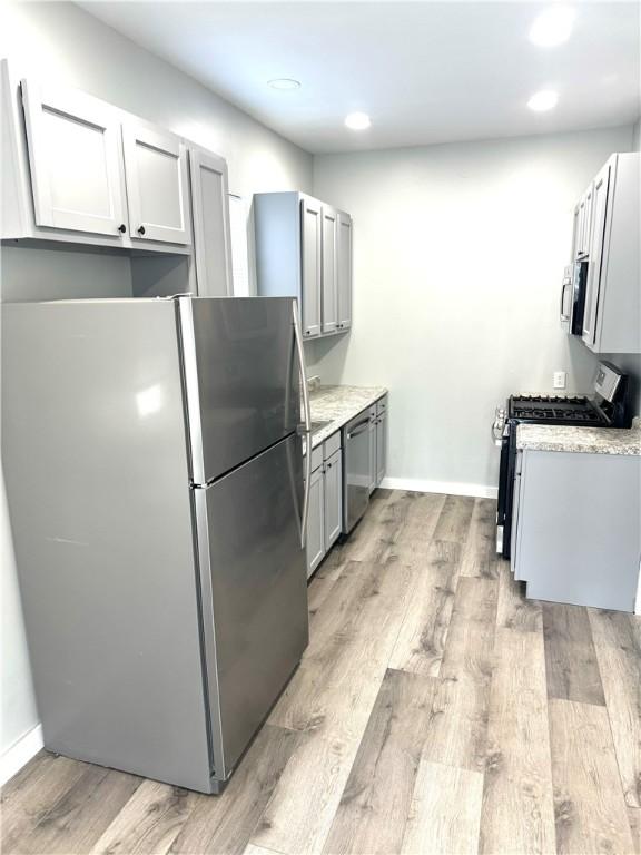 kitchen with gray cabinetry, light stone counters, light hardwood / wood-style flooring, and stainless steel appliances