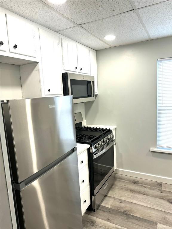 kitchen with appliances with stainless steel finishes, a drop ceiling, white cabinets, and light wood-type flooring