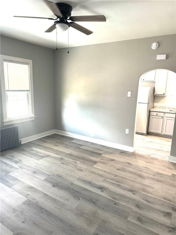 empty room with ceiling fan, radiator, and light wood-type flooring