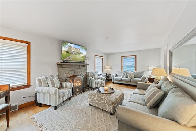 living room with a stone fireplace and light wood-type flooring