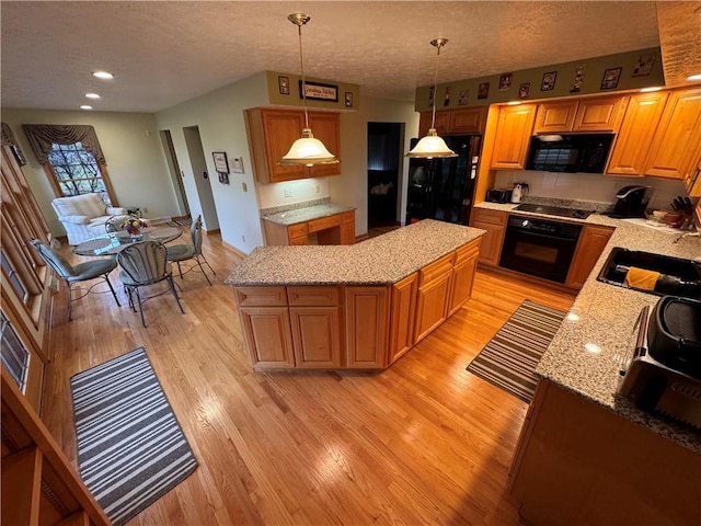 kitchen featuring sink, decorative light fixtures, light wood-type flooring, a kitchen island, and black appliances