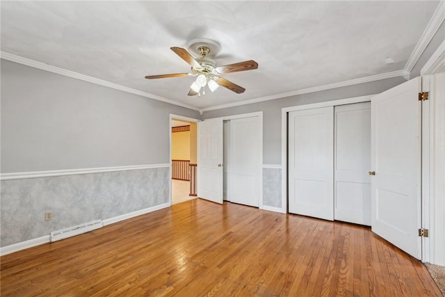 unfurnished bedroom featuring multiple closets, crown molding, hardwood / wood-style flooring, and ceiling fan