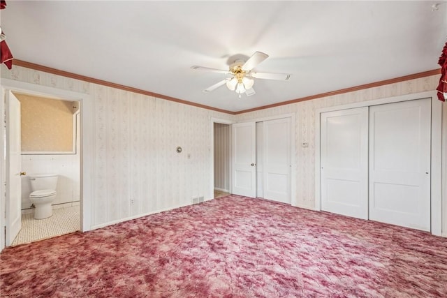 unfurnished bedroom with two closets, ensuite bath, ornamental molding, and carpet