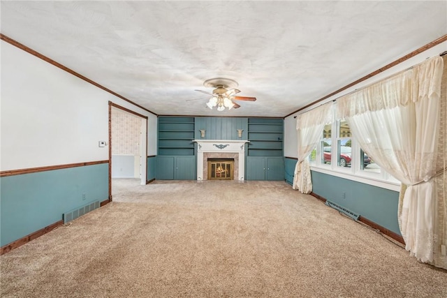 unfurnished living room with a tile fireplace, carpet flooring, ornamental molding, ceiling fan, and a textured ceiling