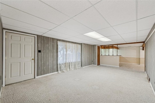 basement with light carpet, wooden walls, and a drop ceiling