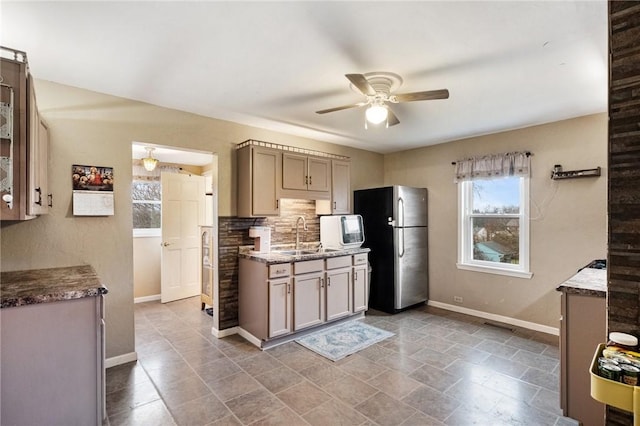 kitchen with ceiling fan, sink, backsplash, and stainless steel refrigerator