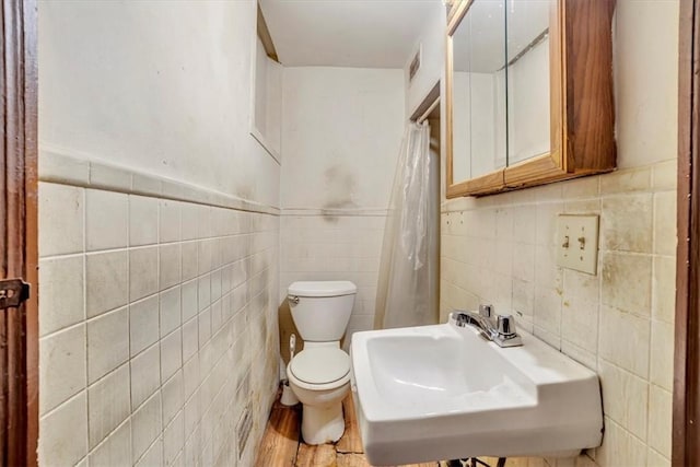 bathroom with toilet, sink, hardwood / wood-style floors, and tile walls