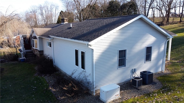 view of side of home with a lawn, cooling unit, and roof with shingles