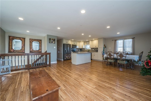 kitchen with appliances with stainless steel finishes, light hardwood / wood-style floors, white cabinets, a kitchen island, and decorative backsplash