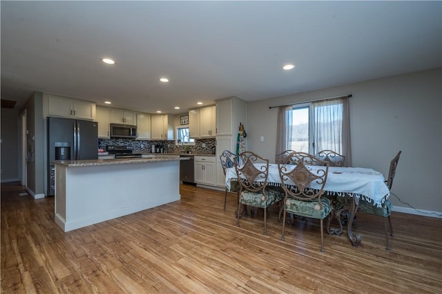 kitchen featuring a kitchen island, tasteful backsplash, white cabinets, stainless steel appliances, and light wood-type flooring