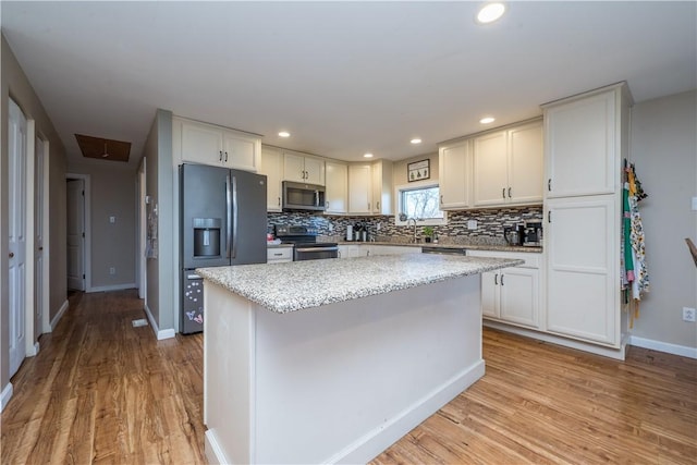 kitchen with stainless steel appliances, white cabinetry, light stone countertops, and a center island