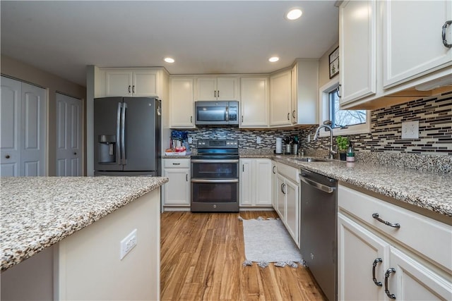 kitchen with white cabinetry, sink, light stone counters, stainless steel appliances, and light hardwood / wood-style flooring