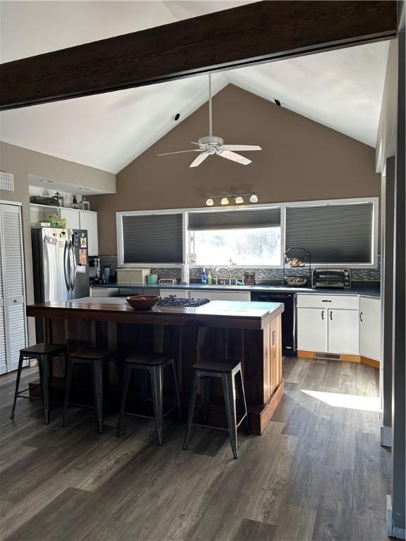 kitchen featuring dark hardwood / wood-style floors, white cabinetry, a breakfast bar area, stainless steel fridge, and beam ceiling