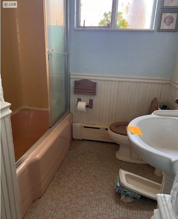 bathroom featuring bath / shower combo with glass door, baseboard heating, and toilet