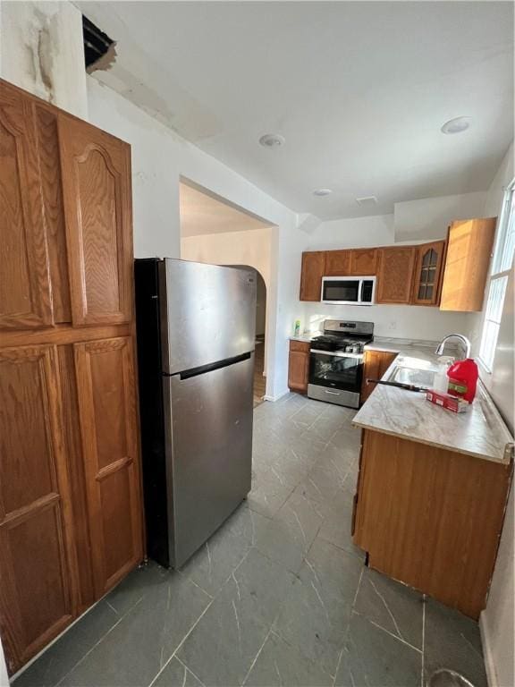 kitchen featuring brown cabinets, stainless steel appliances, light countertops, glass insert cabinets, and a sink