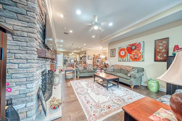 living room with ornamental molding, a stone fireplace, hardwood / wood-style floors, and ceiling fan