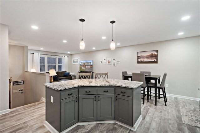 kitchen with a center island, decorative light fixtures, gray cabinets, and light stone countertops