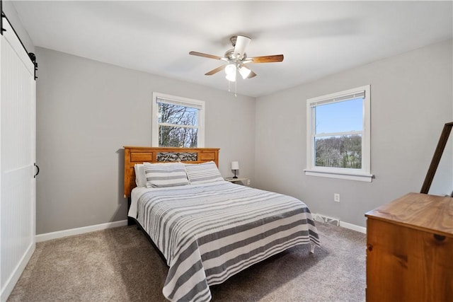 bedroom with a barn door, dark carpet, and multiple windows