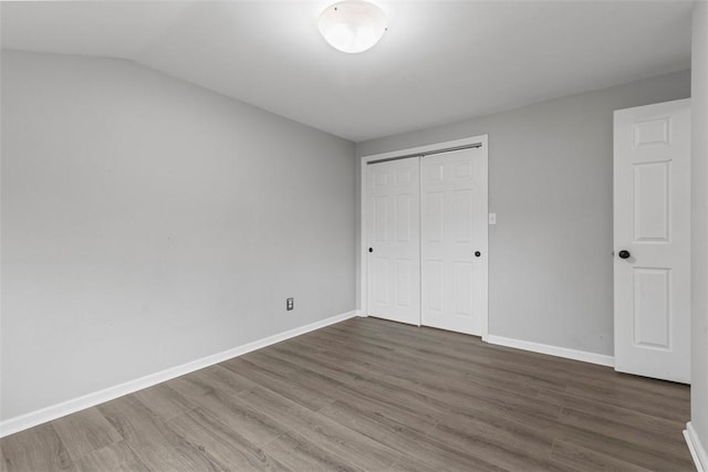 unfurnished bedroom with dark hardwood / wood-style floors, vaulted ceiling, and a closet