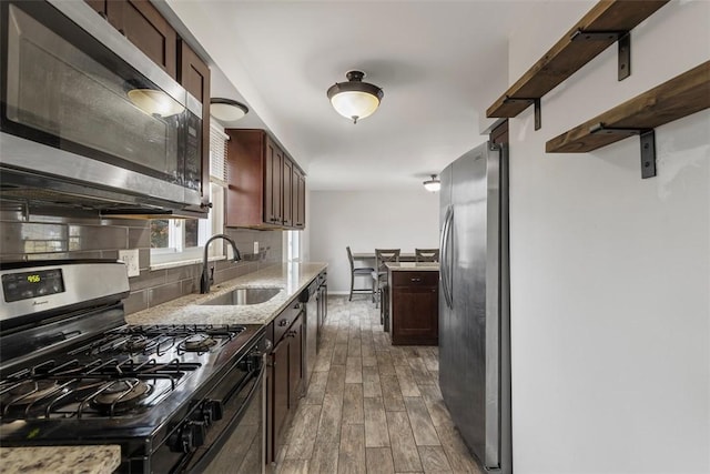 kitchen with sink, dark wood-type flooring, stainless steel appliances, light stone counters, and decorative backsplash