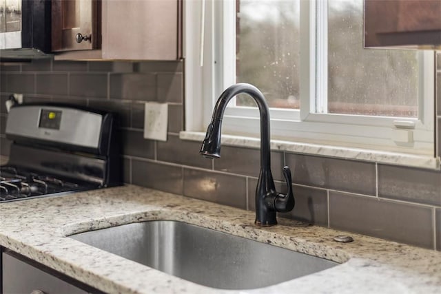 kitchen with tasteful backsplash, sink, light stone counters, and gas range