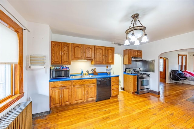 kitchen with pendant lighting, sink, appliances with stainless steel finishes, radiator heating unit, and light wood-type flooring