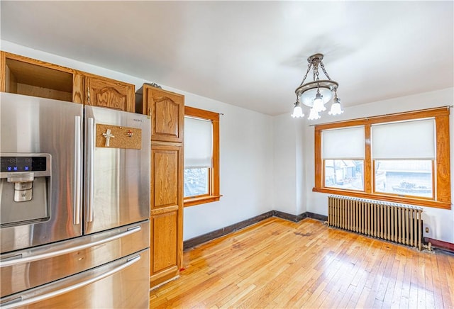 kitchen featuring pendant lighting, radiator, plenty of natural light, and stainless steel refrigerator with ice dispenser