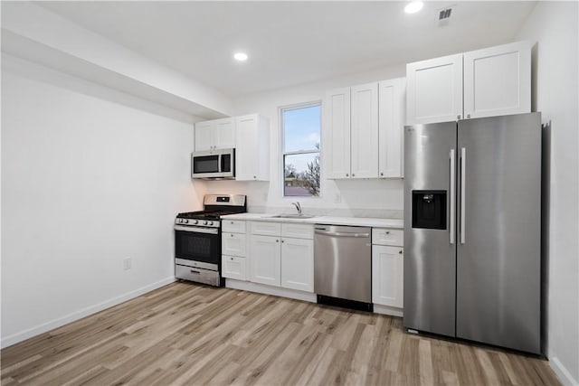 kitchen with stainless steel appliances, white cabinetry, sink, and light hardwood / wood-style flooring