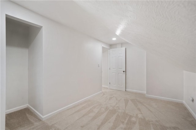 additional living space with light colored carpet, vaulted ceiling, and a textured ceiling