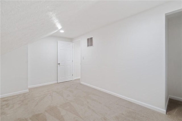 additional living space with vaulted ceiling, light carpet, and a textured ceiling