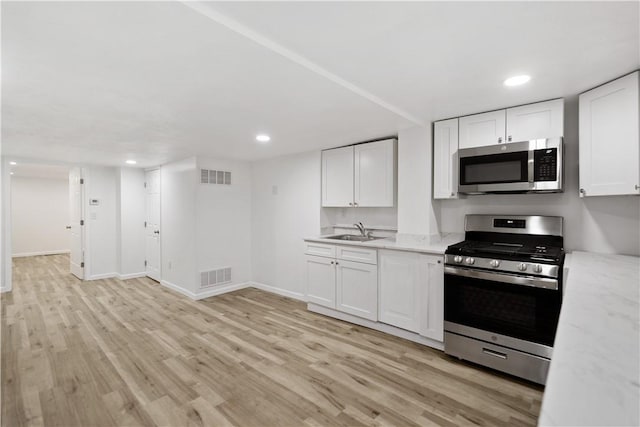 kitchen with light stone countertops, appliances with stainless steel finishes, white cabinets, and light hardwood / wood-style floors