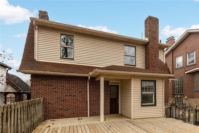 back of house featuring brick siding, a deck, a chimney, and fence