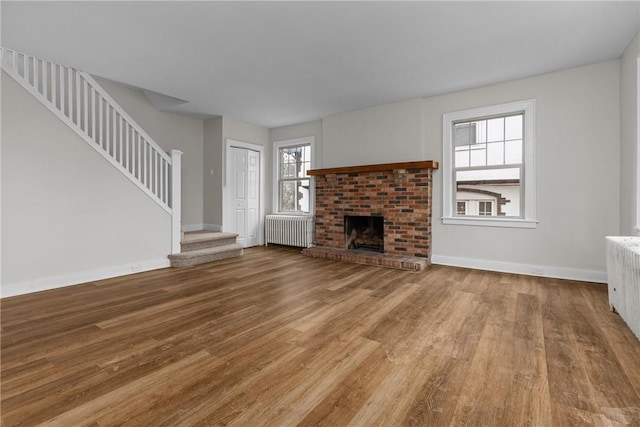 unfurnished living room with wood finished floors, radiator, a fireplace, baseboards, and stairs