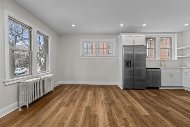 kitchen with appliances with stainless steel finishes, a wealth of natural light, radiator heating unit, white cabinets, and light hardwood / wood-style floors