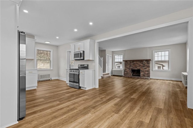 kitchen featuring stainless steel appliances, radiator, open floor plan, and white cabinets