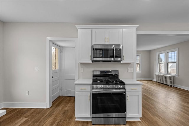 kitchen with light wood finished floors, appliances with stainless steel finishes, light countertops, and radiator heating unit