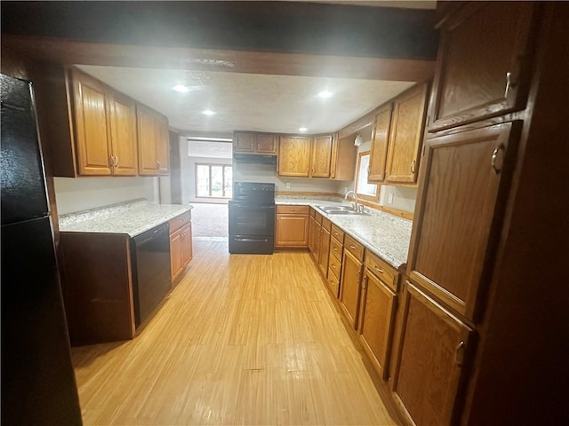 kitchen featuring light stone counters, sink, light hardwood / wood-style flooring, and black appliances