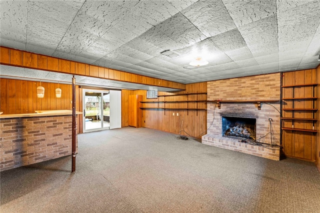 unfurnished living room with a brick fireplace, carpet floors, and wood walls