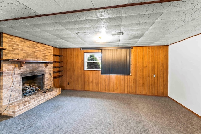 unfurnished living room with a brick fireplace, carpet flooring, and wood walls