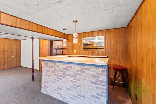 kitchen featuring a breakfast bar area, wooden walls, kitchen peninsula, carpet floors, and pendant lighting