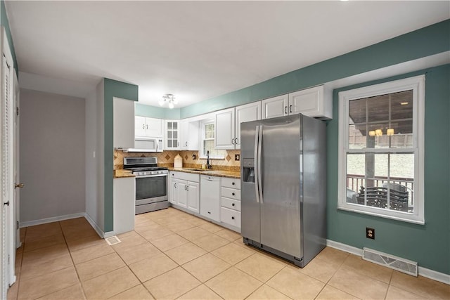 kitchen featuring sink, light tile patterned floors, white cabinets, stainless steel appliances, and backsplash