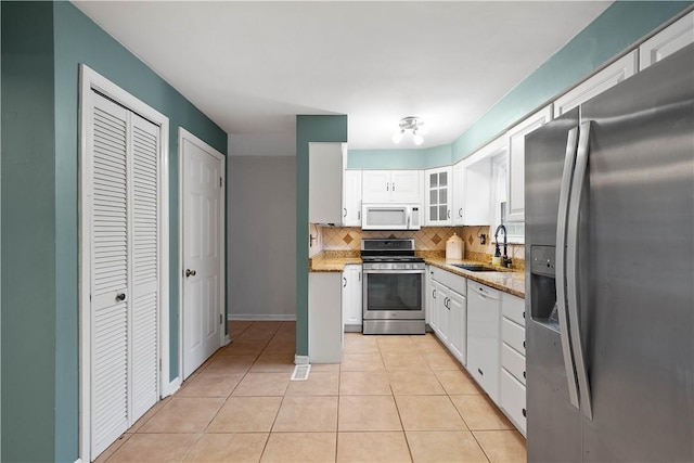 kitchen with sink, light tile patterned floors, appliances with stainless steel finishes, white cabinetry, and tasteful backsplash