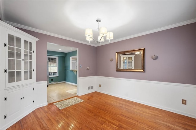 empty room featuring ornamental molding, an inviting chandelier, and light hardwood / wood-style flooring